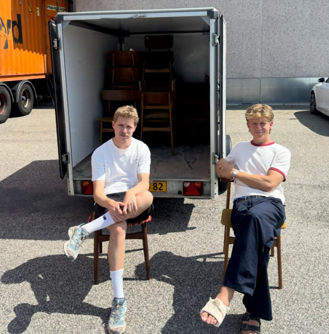 To af stifterne sidder på stole foran en trailer fuld af barstole