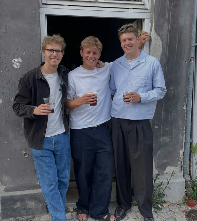 De tre stiftere med hver sin fadøl foran døren til baren